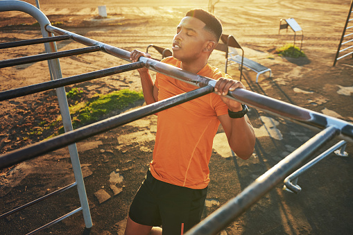 Shot of a young man working out at the outdoor gym at the park