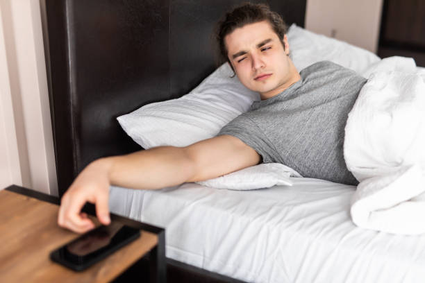 istock Handsome young man waking up with mobile alarm clock 1307388915
