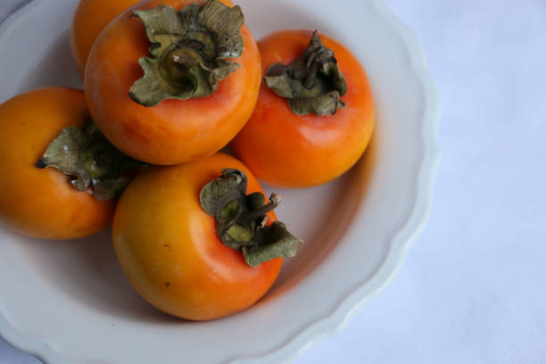 istock Fresh Ripe Persimmons on a White Classic Design Plate, Paradise Palms 1307392555
