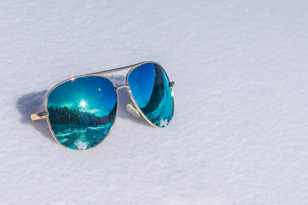 occhiali da sole con lenti blu in cui il sole e la foresta si riflettono giacciono sulla neve - snow glasses foto e immagini stock