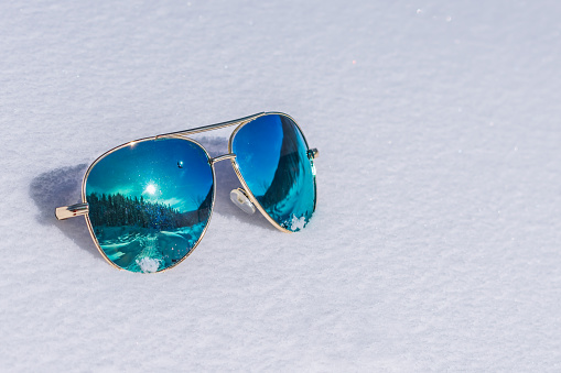 Sunglasses with blue lenses reflecting the sun and the forest