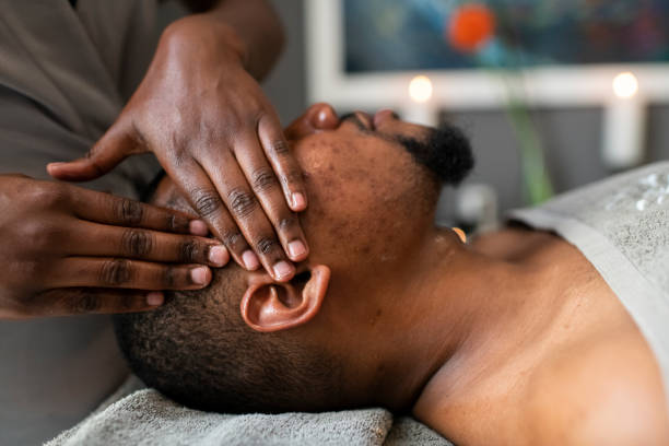 Masseuse giving head massage to man in spa Masseuse giving head massage to patient at a spa black male massage stock pictures, royalty-free photos & images