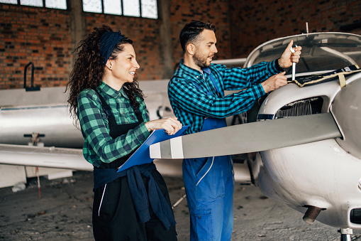 Young couple running their own flying school business. They are checking and repairing small propeller airplane in airport hangar.