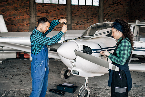 Young couple running their own flying school business. They are checking and repairing small propeller airplane in airport hangar.