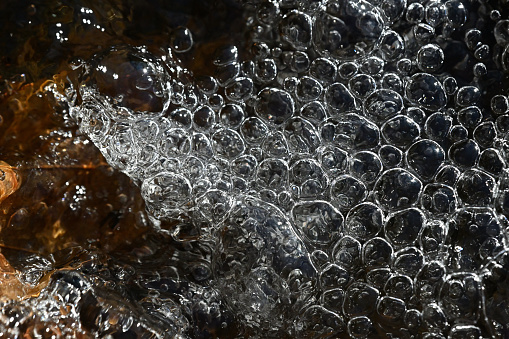 Bubbles forming funnel in shallow stream on hillside in the woods of New England, with oak leaves in the stream bed