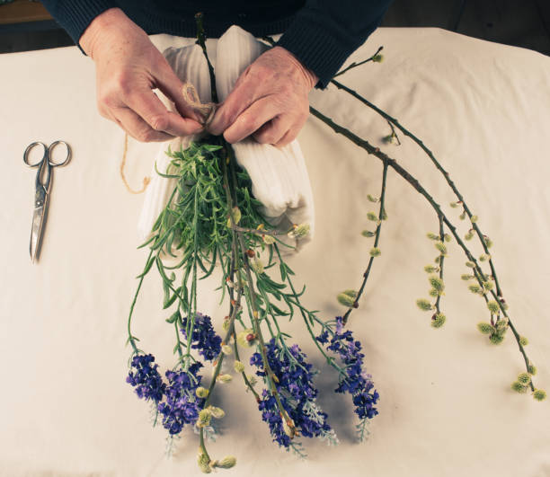 istock DIY, Female hand with violet flowers and willow branches on a table surface, top view. 1307402916