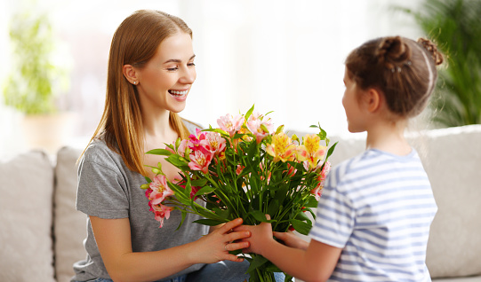 Delighted cute daughter giving bouquet of Alstroemeria flowers to mother on 8 March