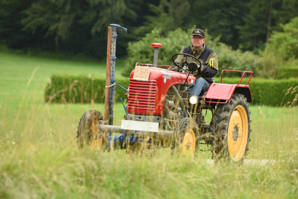 A farmer driving with an old red Steyr tractor on a green meadow at a vintage tractor meeting in Aurach, Vöcklabruck district, Austria, Europe