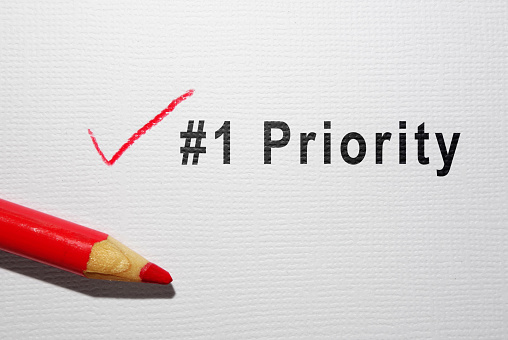 Number one Priority text with red pencil checkmark on paper