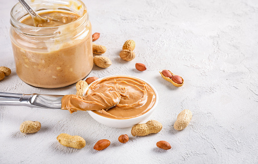 Glass jar full and small bowl full with tasty peanut butter on white background. on white background. Copy space.