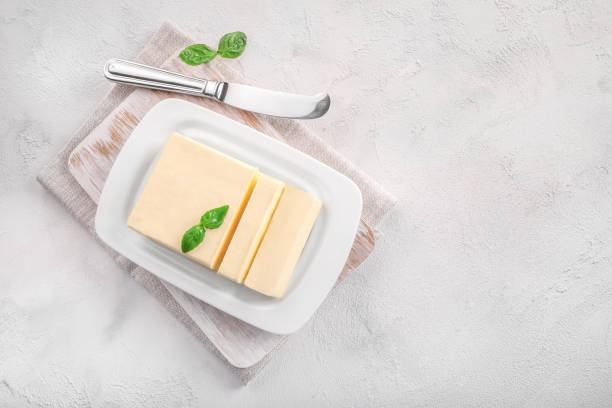 corte o bloco de manteiga fresca em prato de manteiga de cerâmica branca no fundo branco. - butter dairy product butter dish milk - fotografias e filmes do acervo