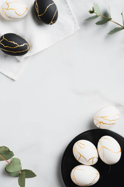 istock Frame of white and black Easter eggs decorated gold and eucalyptus leaves on marble table. Flat lay, top view. Happy Easter vertical banner design. 1307409922