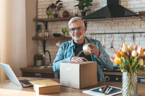 istock Send a parcel. A bearded elderly man volunteer packing a donation carton in the kitchen. Home office, small business 1307410026