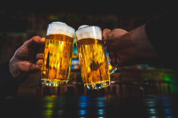 vista de cerca de dos vasos de cerveza en la mano. vasos de cerveza clinking en bar o pub - clunking fotografías e imágenes de stock