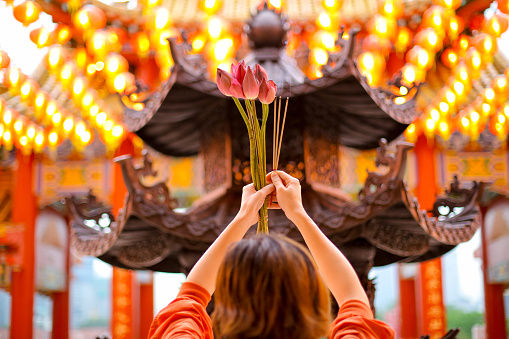 An Asian woman is holding fresh lotus flower and incense sticks praying at Thean Hou Temple, Kuala Lumpur Malaysia.