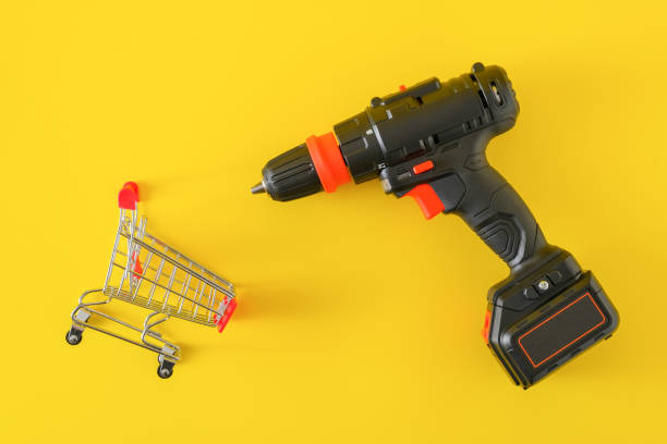 Modern black cordless screwdriver with empty shopping cart Modern black cordless screwdriver, drill with empty shopping cart on yellow background, top view chuck wagon stock pictures, royalty-free photos & images