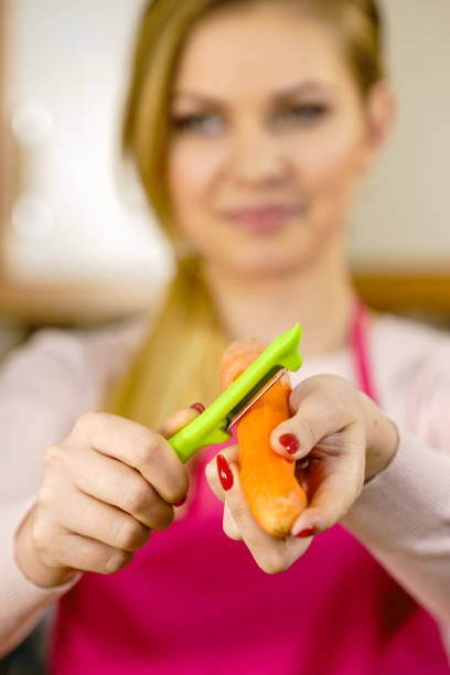Woman peeling vegetables using food peeler. Cooking female preparing carrot before serving.