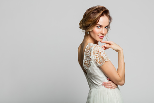 Smiling blond woman wearing weeding dress standing against grey background. Studio shot.