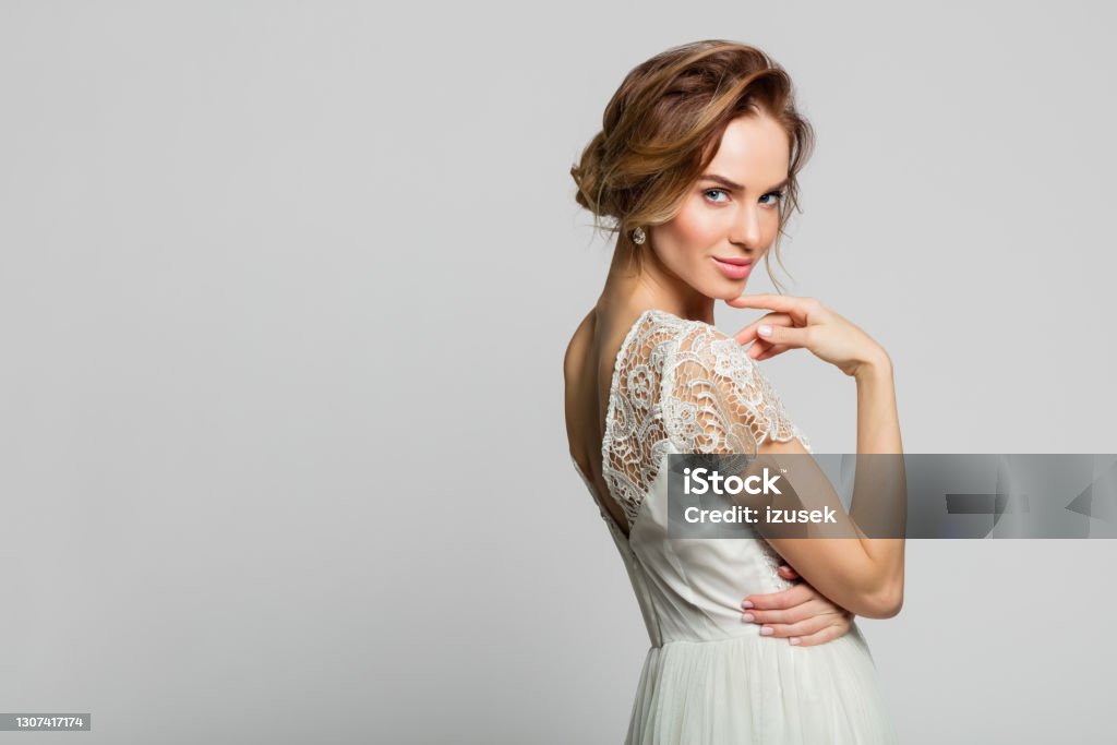 Portrait of beautiful bride Smiling blond woman wearing weeding dress standing against grey background. Studio shot. Beauty Stock Photo
