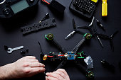 Close up of man's hands assembling a FPV drone from parts, using tools, Preparing high-speed racing quadcopter for flight. Repair drone before training process.