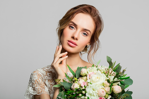 Blond woman wearing weeding dress and holding bouquet. Studio shot against grey background.