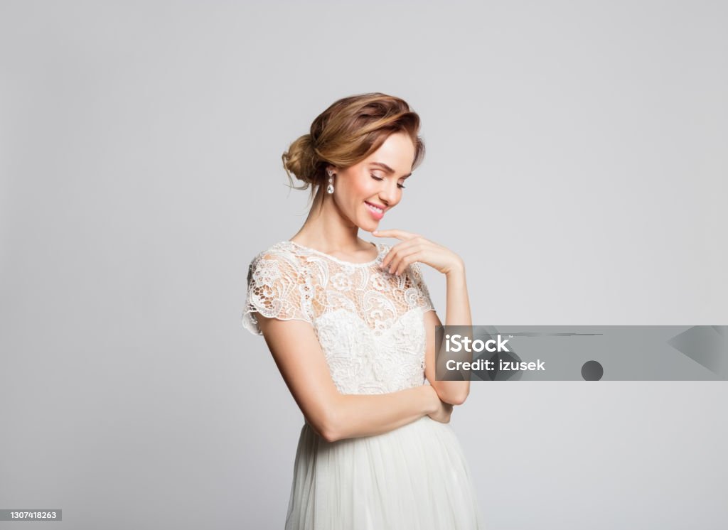 Portrait of beautiful bride Happy blond woman wearing weeding dress standing against grey background. Studio shot. Lace - Textile Stock Photo