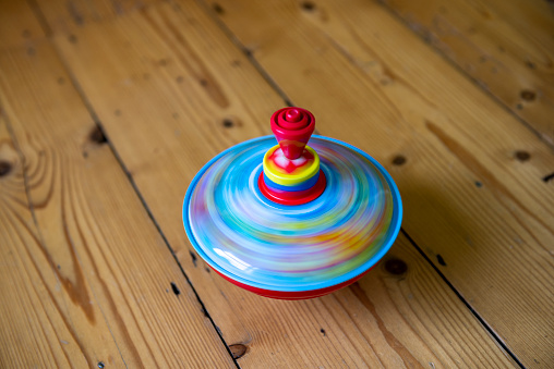A colourful child's toy spinning top on a wooden floor spinning fast so as to create motion blur.