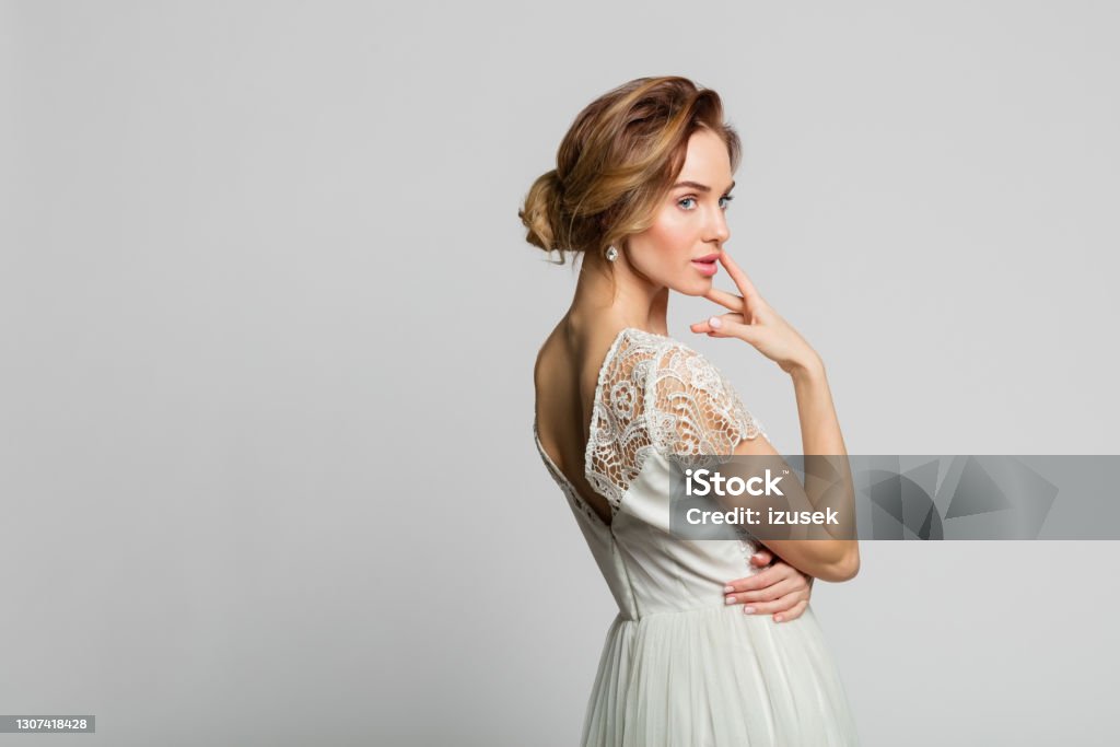 Portrait of beautiful bride Thoughtful blond woman wearing weeding dress standing against grey background. Studio shot. Rear View Stock Photo