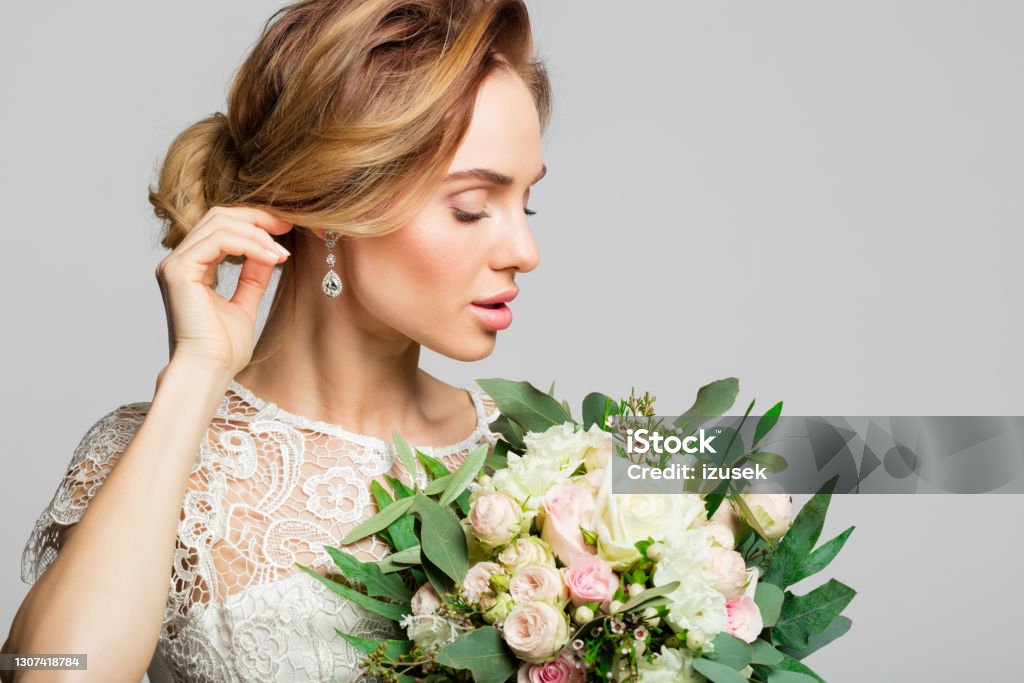 Portrait of beautiful bride Side view of blond woman wearing weeding dress and holding bouquet. Studio shot against grey background. Adult Stock Photo