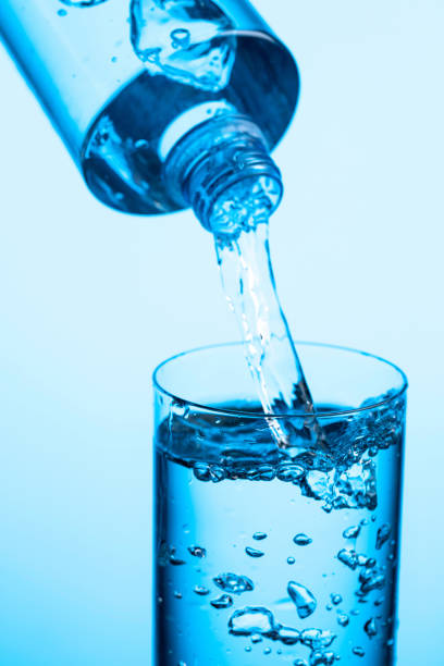 istock Pouring water from a bottle into glass on a blue background. 1307418795