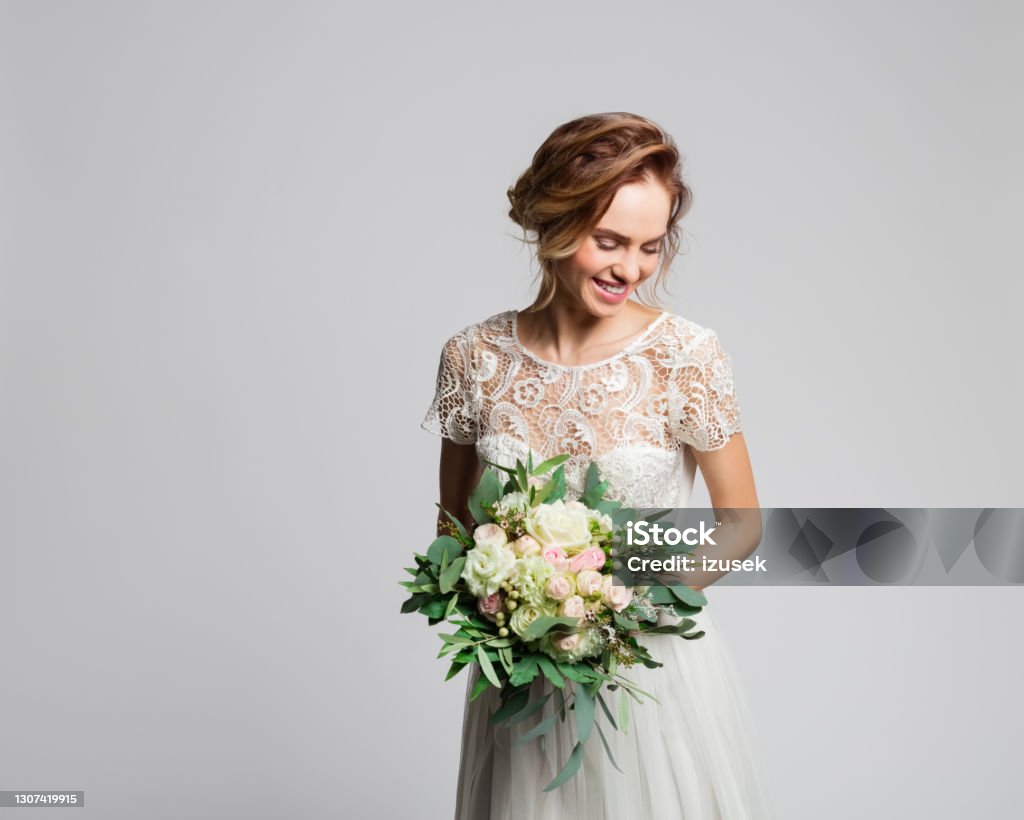Portrait of beautiful bride holding flowers Happy blond woman wearing weeding dress and holding bouquet. Studio shot against grey background. Bride Stock Photo
