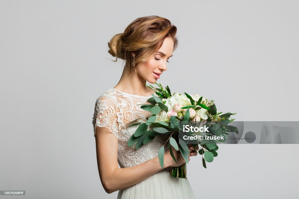 Portrait of beautiful bride holding flowers Blond woman wearing weeding dress and holding bouquet. Studio shot against grey background. Bride Stock Photo