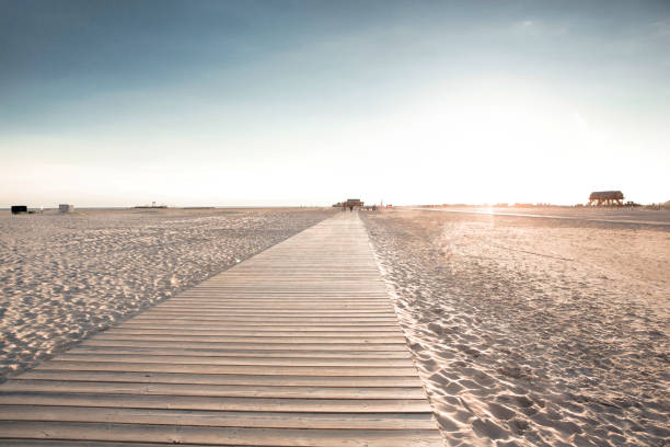 Wooden boardwalk on sandy beach. Many footprints in sand after rush summer day on seaside. Evening view against sunshine.