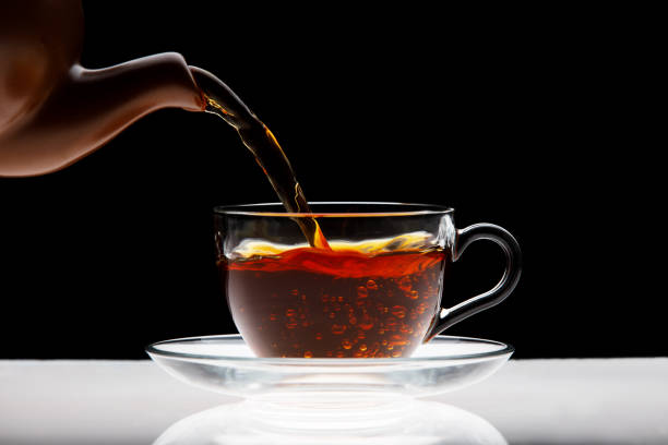 Pouring black tea into transparent cup isolated Pouring black tea into transparent cup isolated on black background black tea stock pictures, royalty-free photos & images