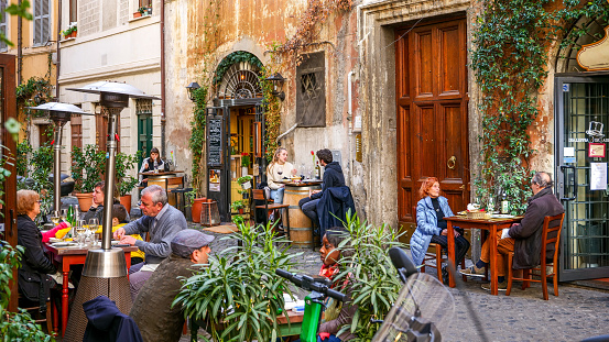 Rome, Italy, March 14 -- Numerous customers seated in some picturesque and lovely Italian restaurants along the alley of Via Dei Cappellari, near Campo de Fiori square, in one of the most visited districts of the Eternal City, with the facades of ancient and noble palaces in warm pastel tones, typical restaurants, alleys and large pedestrian areas. Image in high definition format.