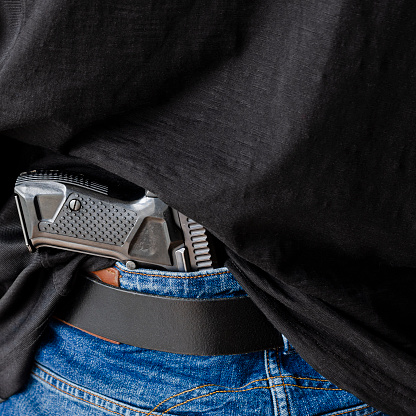 A person is hiding a handgun under the denim belt. Hided handgun under the denim belt.