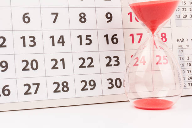 istock Time passing concept. Crystal hourglass with red sand and calendar on light background 1307424019