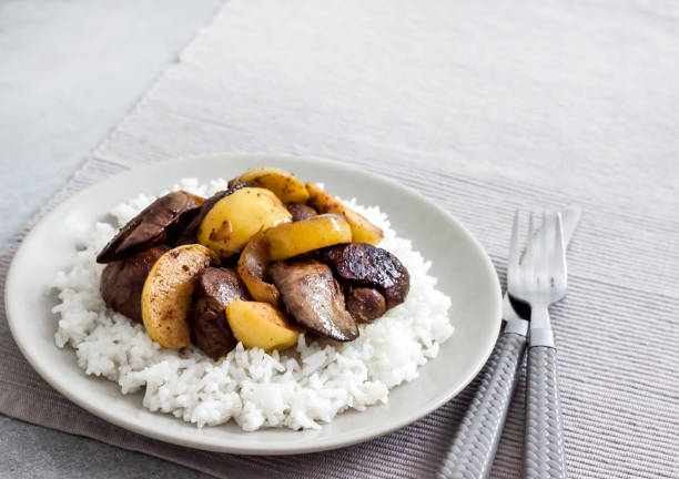 Fried chicken liver with apples served with white rice on a plate. Green apples on background. Copy space
