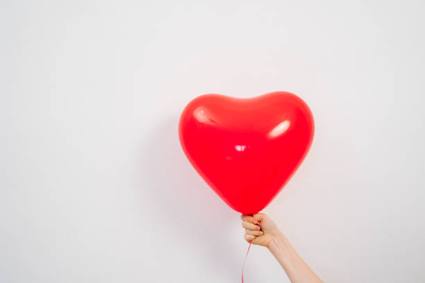 istock A heart shaped red balloon in hand against a white wall. 1307432605