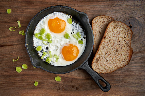 Flat lay shot of fried eggs with rye bread in a cast iron skillet on wooden board