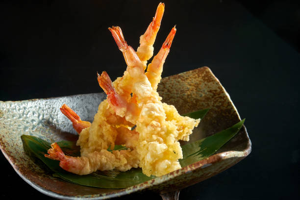обжаренные креветки. креветки фри в темпуре, подается в че�рной миске в японском стиле. изолирован на черном фоне. ресторанная еда - морепрод� - tempura стоковые фото и изображения