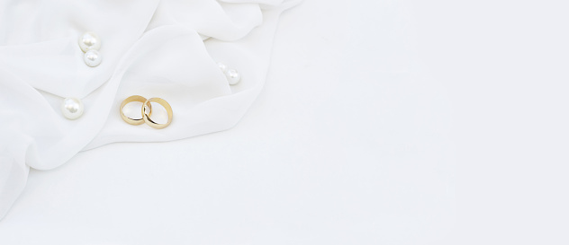 Two golden wedding rings and pearls on white background.	Wedding banner