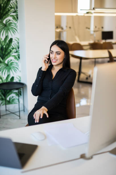 istock Business woman working on laptop at office while talking on phone 1307452192