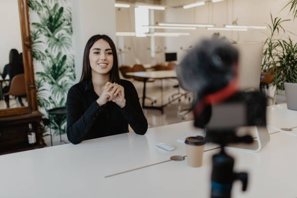 istock Young woman vlogger while recording her daily video blog. Vlogger using a camera mounted on a tripod to record her video. 1307453901