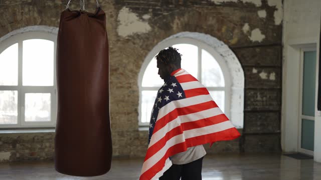 Afro American boxer coming to a boxing studio with american flag on shoulders