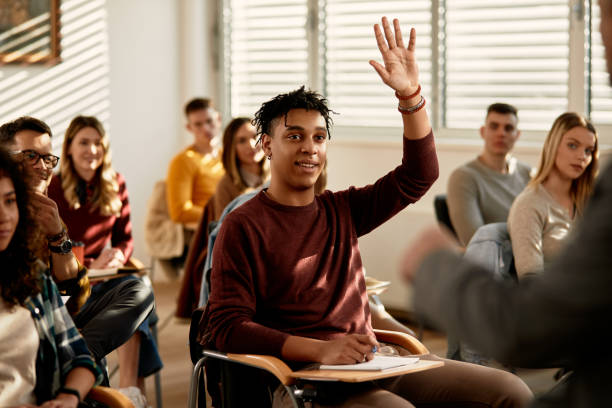 Happy black student raising arm to answer a questing in the classroom. Smiling African American student raising his hand to ask a questing during a class at lecture hall. hand raised classroom student high school student stock pictures, royalty-free photos & images