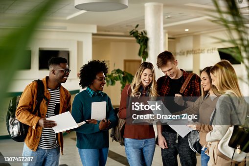 istock Group of happy students looking at exam results while standing at university hallway. 1307457287