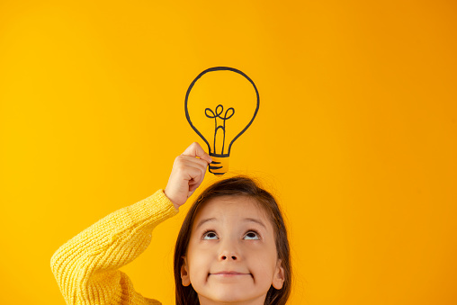 Hand holding light bulb on head against yellow background.
