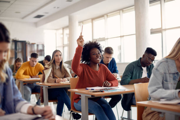 Happy black student raising arm to answer question while attending class with her university colleagues. Happy African American student raising her hand to ask a question during lecture in the classroom. learning stock pictures, royalty-free photos & images