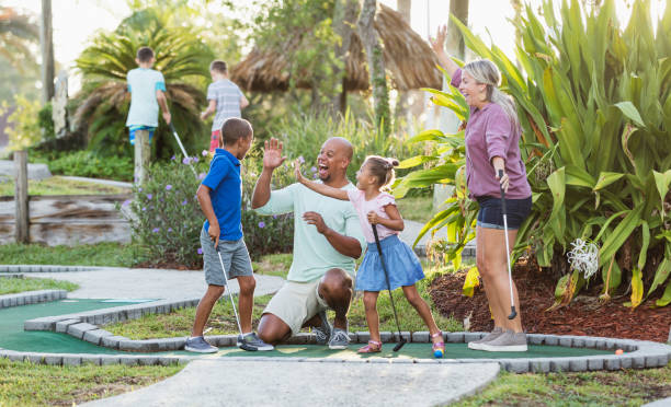 interracial familie, zwei kinder spielen minigolf - putting stock-fotos und bilder